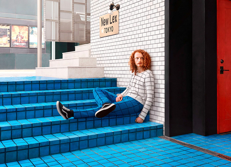 A man in a gridded sweater that matches the gridded wall behind him