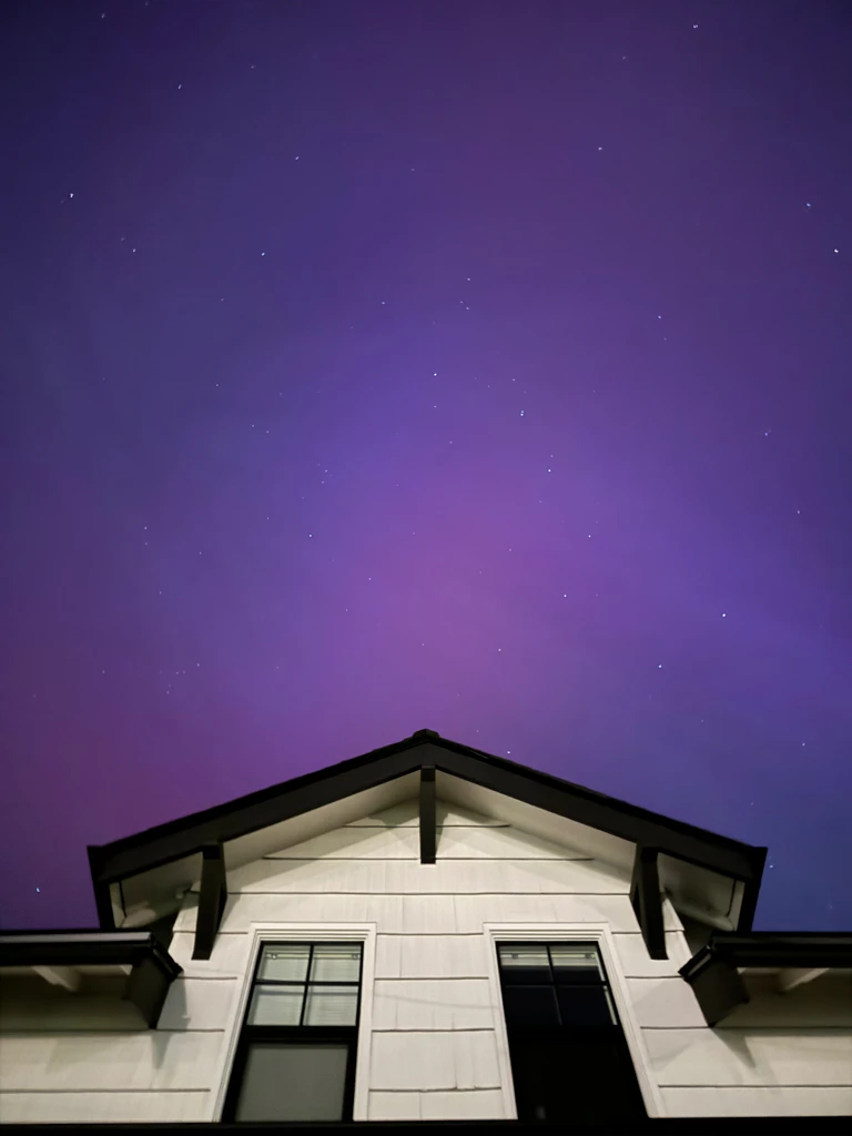 A deep, cooler purple sky beyond the peak of my house. More of a gradient than any sort of shape. Stars stud the aurora, including the big dipper.