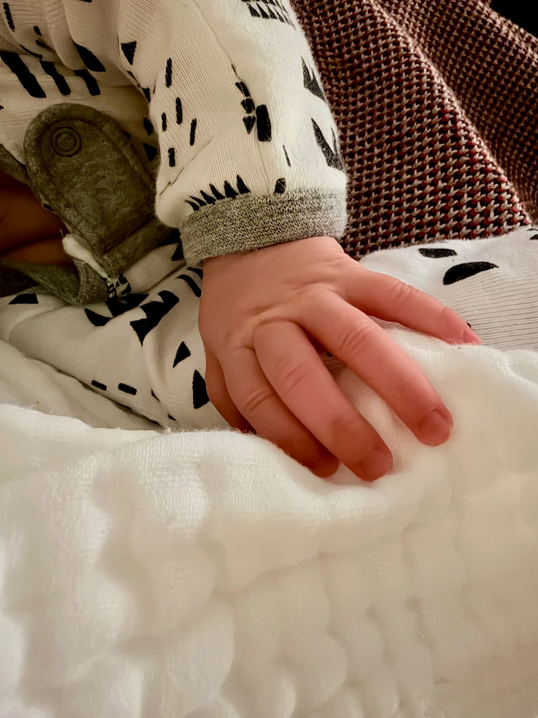 A tiny baby hand resting on a white burp cloth