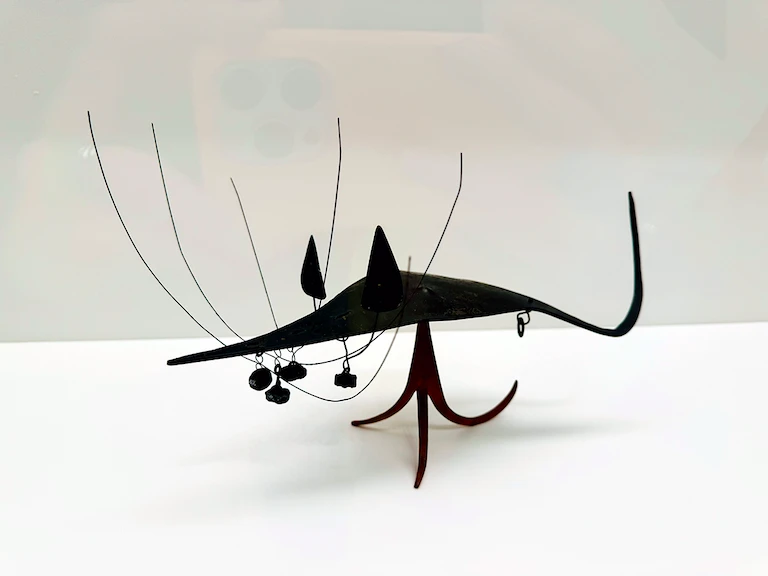 A small, black, metal mouse with enormous whiskers curling upwards. The whiskers are as tall as its body, giving this sculpture twice the height overall.