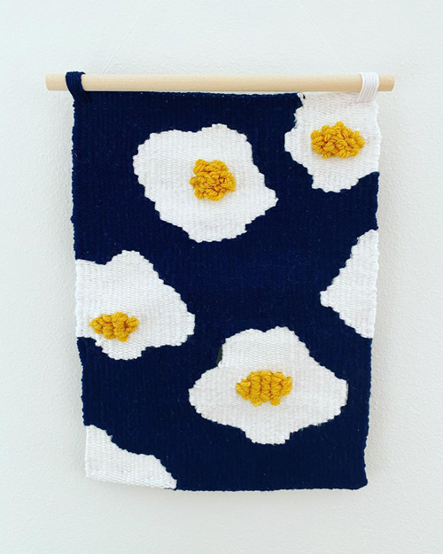 A tapestry featuring fried eggs with fluffy yokes on a navy background