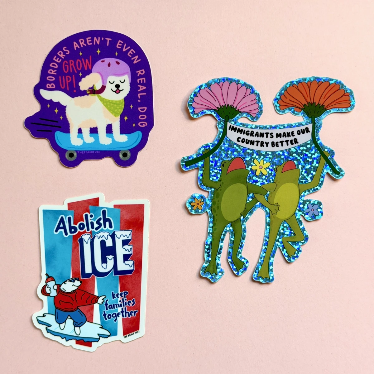 A collection of three stickers about immigration. There is a small skateboarding dog saying 'Borders arent even real, dog. Grow up!' There are two sparkly frogs holding a banner between two flowers, which reads 'Immigrants make our country better'. And there is a riff on the ICEE machine label with a polar bear labeled 'Abolish ICE, keep families together'.