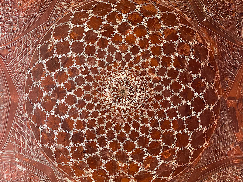 A terracotta mosque ceiling with an intricate white design inside a large circle