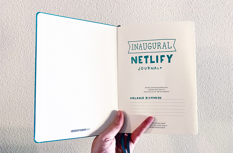 A teal journal opened to the first page, where I have written in teal pen 'Inaugural Netlify journal'