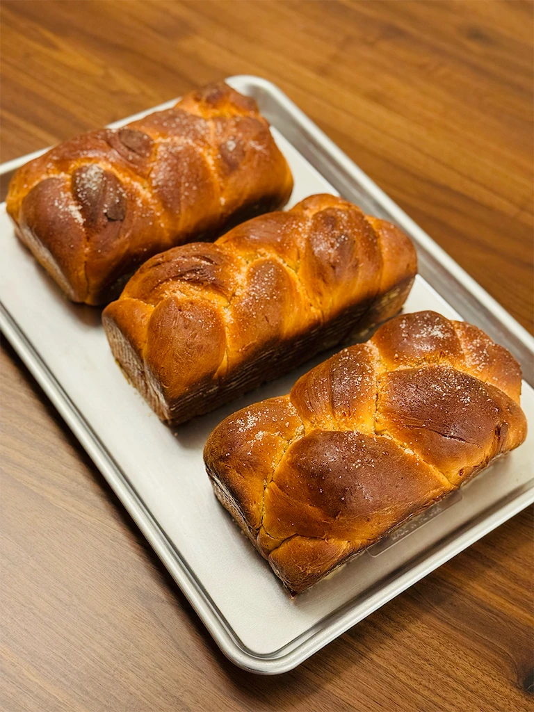 Three golden-brown braided loaves lined up in a rowAlt