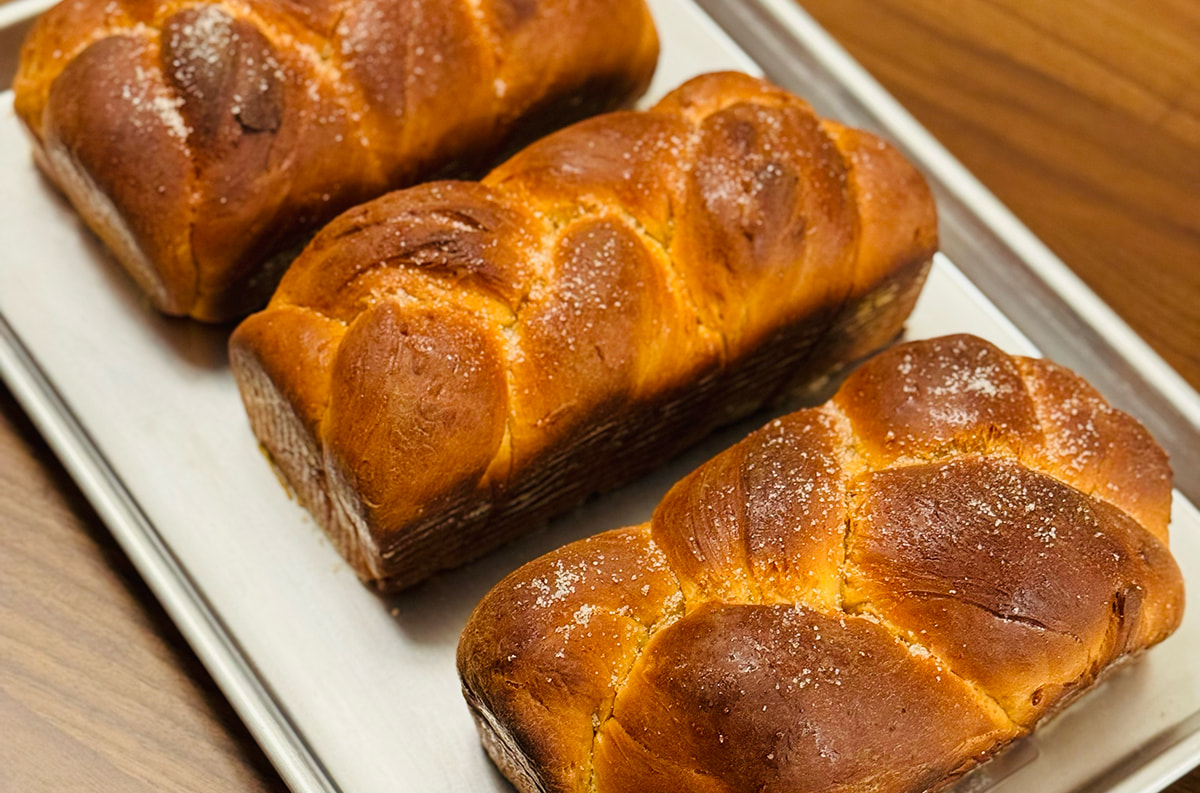 Three golden-brown braided loaves lined up in a row