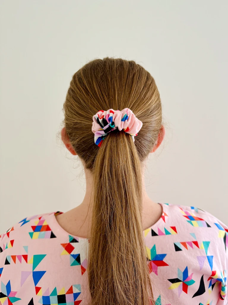 I made a PJ top in a pink cotton with abstract, colorful quilty shapes printed on it. This photo shows the back of my head so that you can see a matching pink scrunchie holding my ponytail.