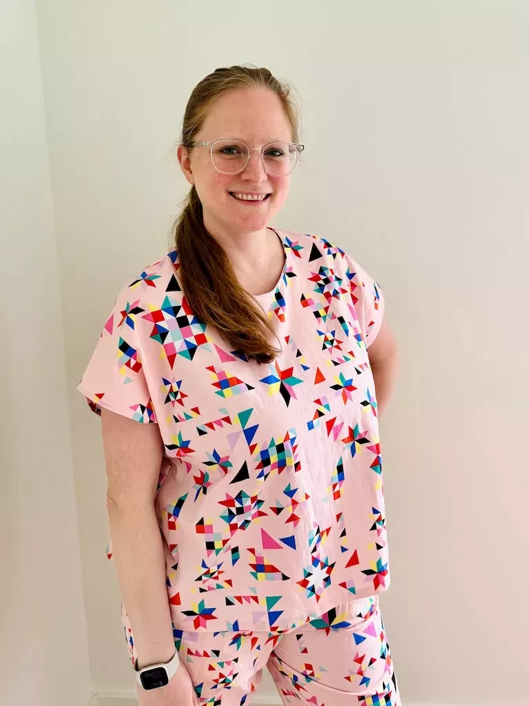 I am wearing a pale pink cotton PJ top that has a pattern of scattered geometric quilt blocks on them. The top matches the PJ bottoms I'm wearing, and the effect is almost like nurse's scrubs.