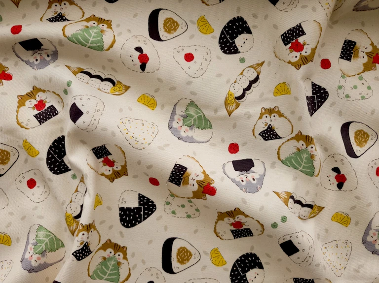 A cream fabric with a pattern of illustrated hamsters in triangular shapes, like onigiri. They're holding up things like a shiso leaf or a strip of nori.